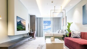 Une chambre d’hôtel moderne avec un grand lit, un canapé rouge, un bureau et une grande fenêtre avec des rideaux.