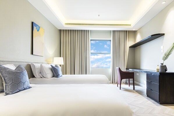 A hotel room with two beds, a desk, and a view of the sky.