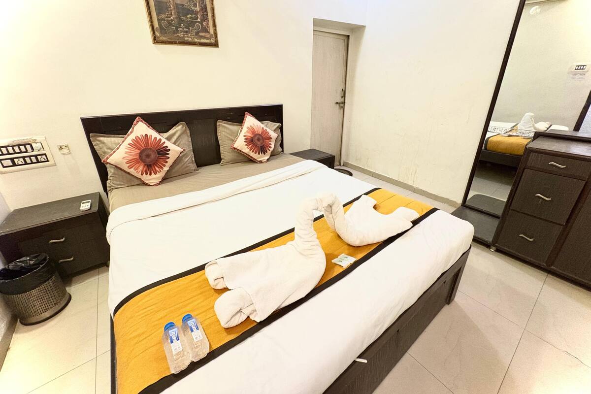Una habitación de hotel con una cama grande, una mesita de noche, un tocador, un espejo, un aparador y un cuadro en la pared.