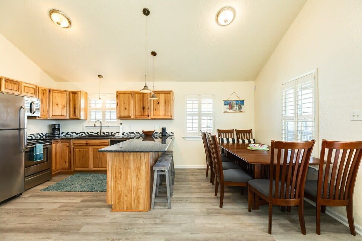 Una cocina con armarios de madera, una isla central, una mesa de comedor con sillas y un refrigerador.