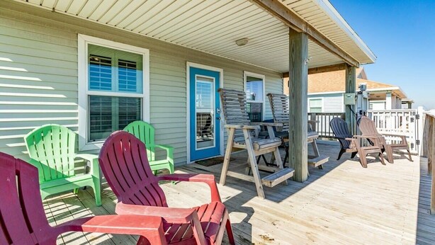 A wooden deck with Adirondack chairs and a table, overlooking a beach.