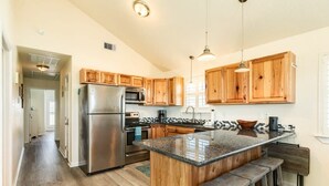 A modern kitchen with wooden cabinets, stainless steel appliances, a granite countertop, and bar stools.