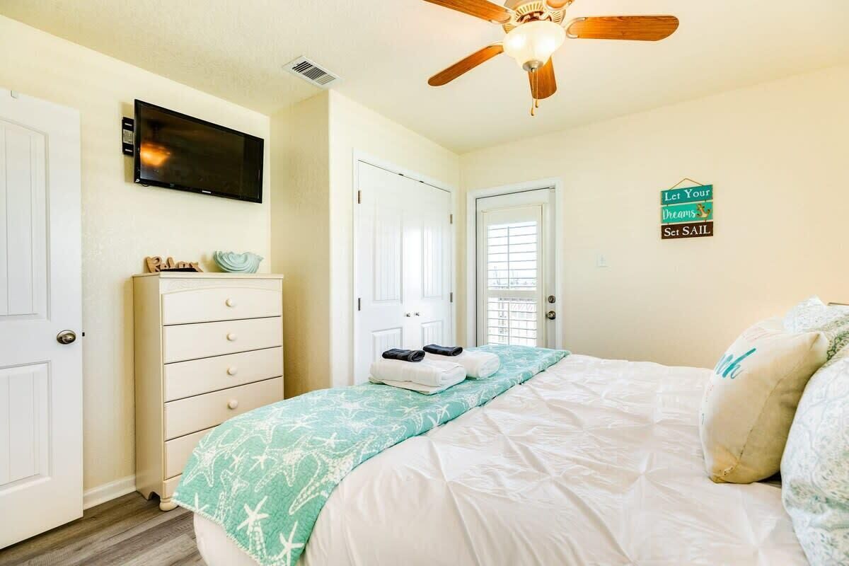 A bedroom with a bed, a ceiling fan, a television, a dresser, and a door.