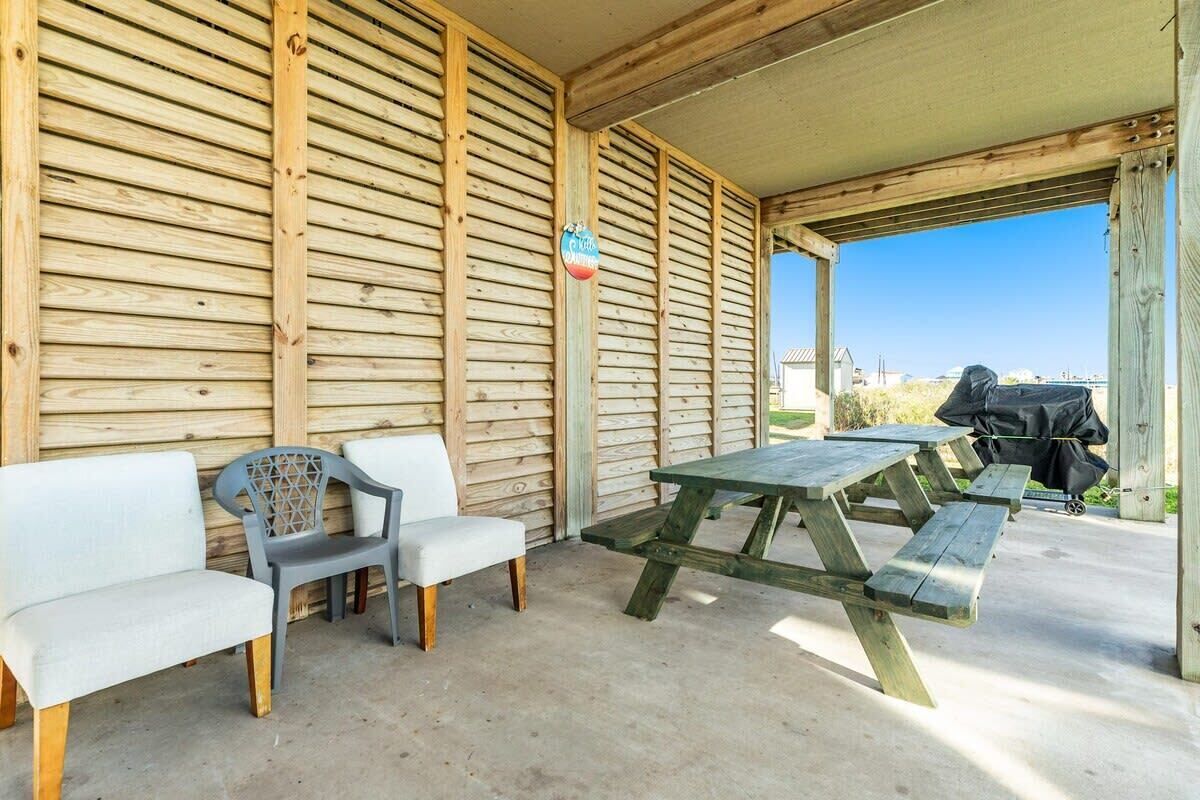 An outdoor seating area with wooden benches and a picnic table, a covered shelter, and a barbecue grill.