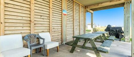 An outdoor seating area with wooden benches and a picnic table, a covered shelter, and a barbecue grill.