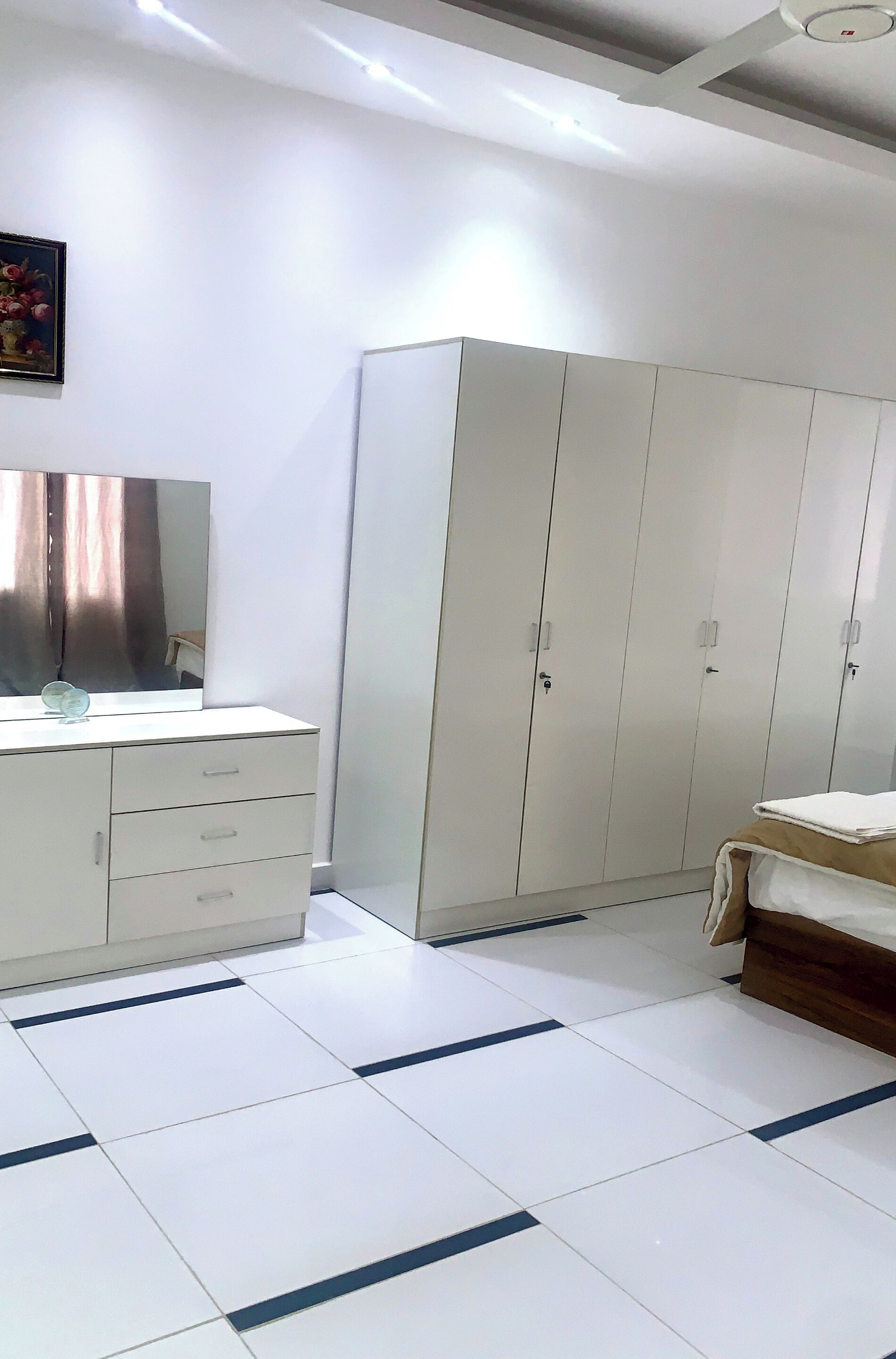 A bedroom with a white wardrobe, a bedside table, and a large mirror.
