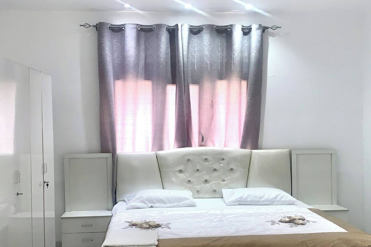 A bedroom with a bed, a ceiling fan, curtains, and a nightstand.