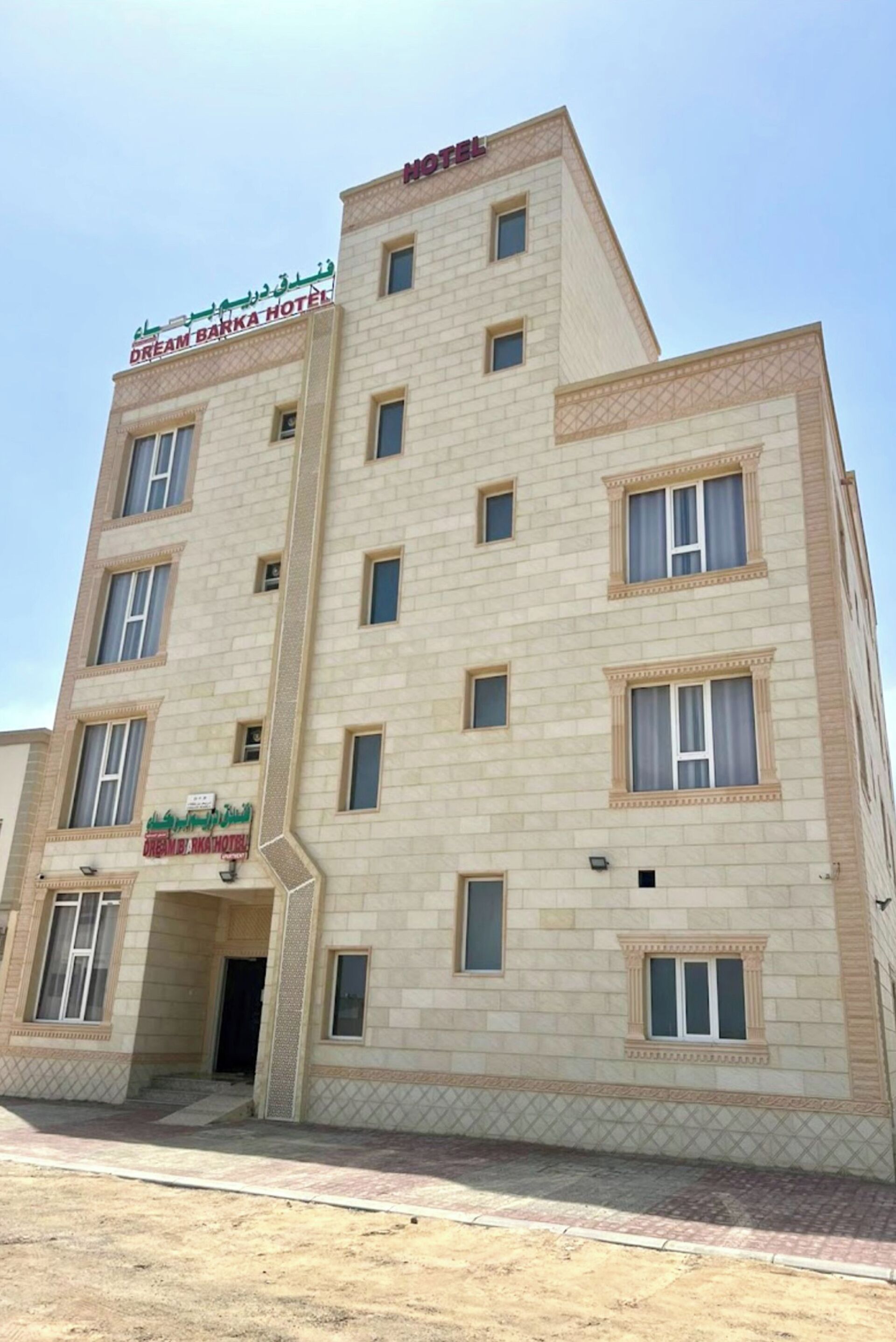 A multi-story hotel with a beige facade, multiple windows, and a sign indicating it is the Dream Barka Hotel.