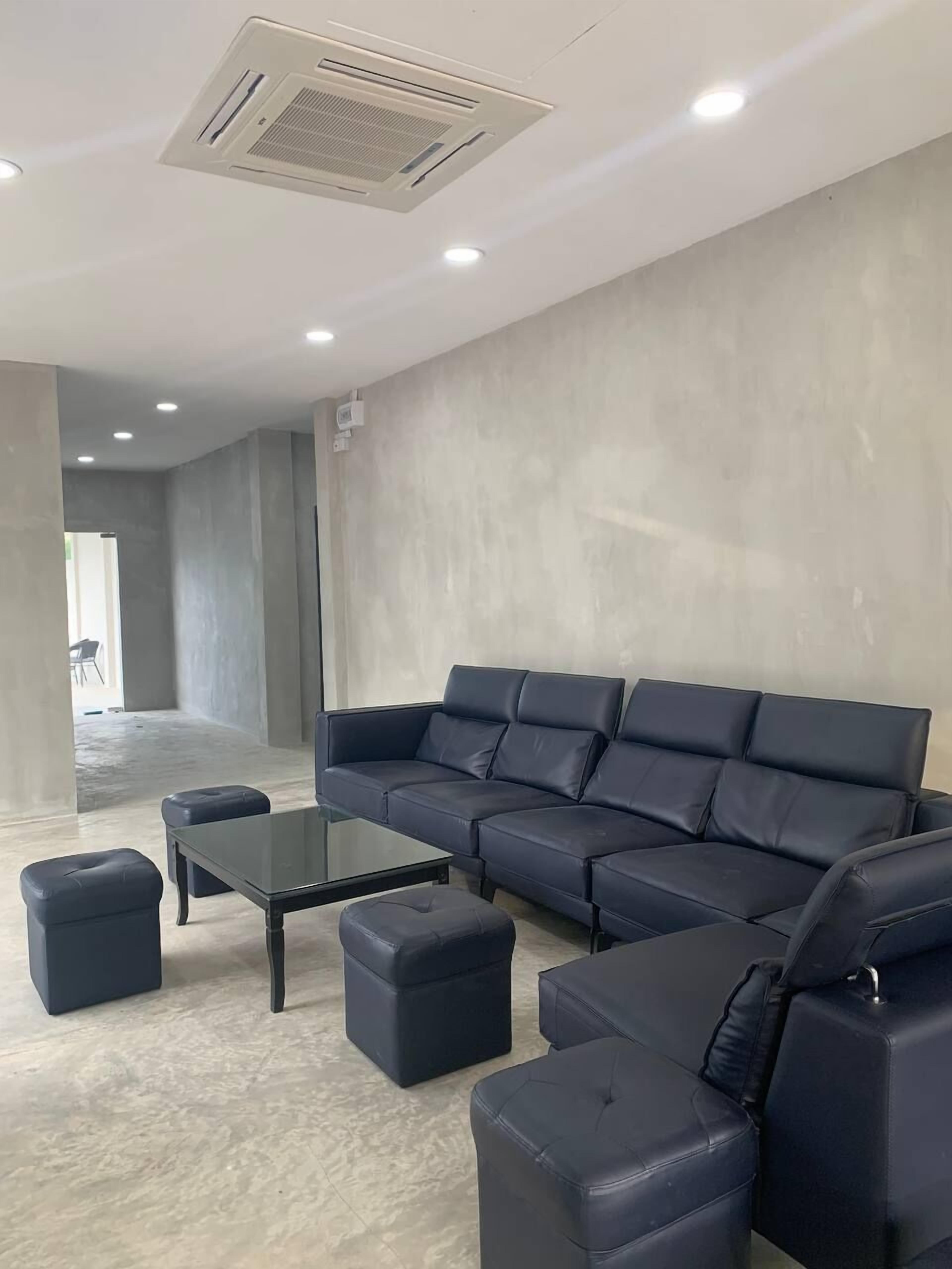 Un salon moderne avec un canapé d’angle, une table basse en verre et des poufs assortis.