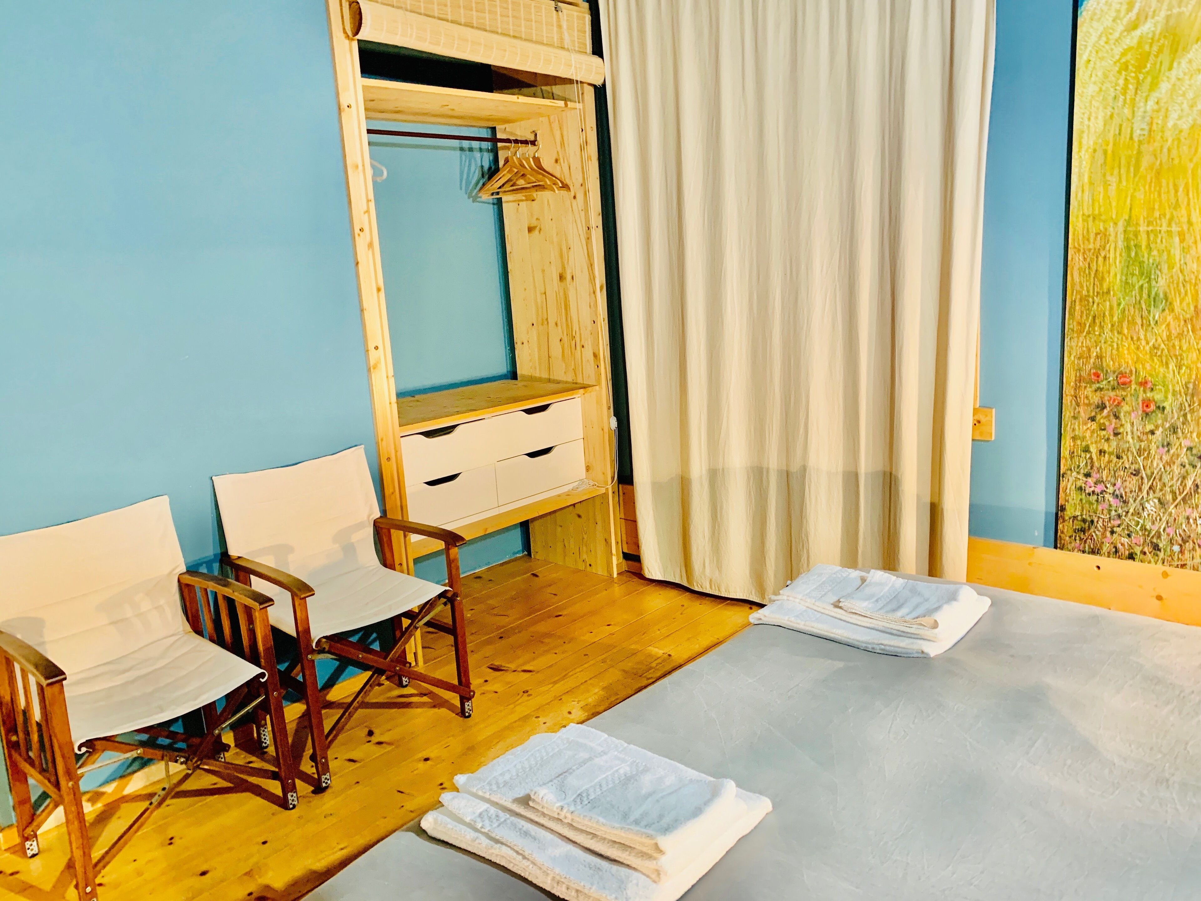 Una camera da letto con un'armadio in legno, un letto con lenzuola bianche, una sedia di legno e un quadro appeso al muro.