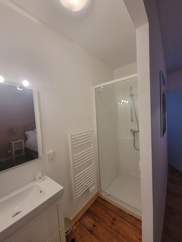 Un baño con lavamanos blanco, espejo y cabina de ducha de vidrio.