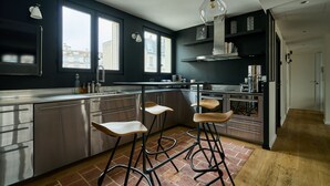 Una cocina moderna con electrodomésticos de acero inoxidable, taburetes de madera y ventanas amplias.