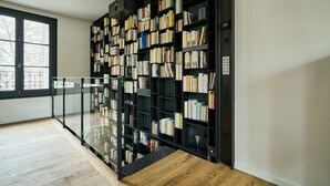 Una biblioteca moderna con una amplia estantería llena de libros, barandilla de vidrio y piso de madera.