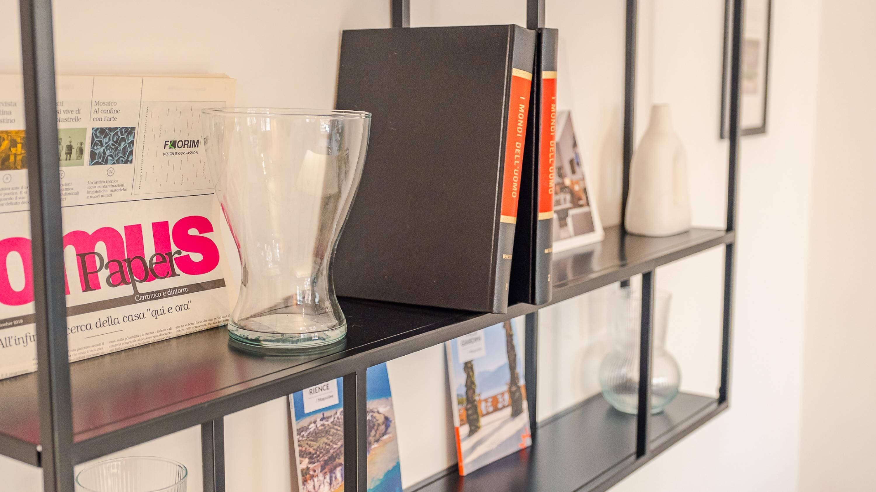 A bookshelf with magazines, a glass vase, and a black box.