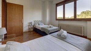 A bedroom with a large bed, a wooden door, a small table with a lamp, and a window with a view of trees. - Colombo 76 in Firenze (Florence)