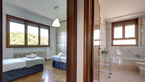 A bedroom with two beds, a wooden floor, and a window with a view of trees. - Colombo 76 in Firenze (Florence)
