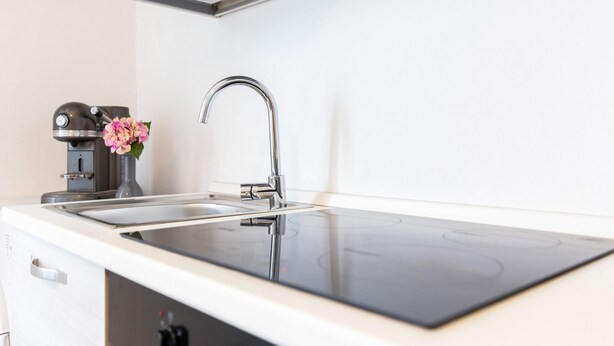 A modern kitchen with a stainless steel sink, a built-in coffee maker, and a black induction cooktop.
