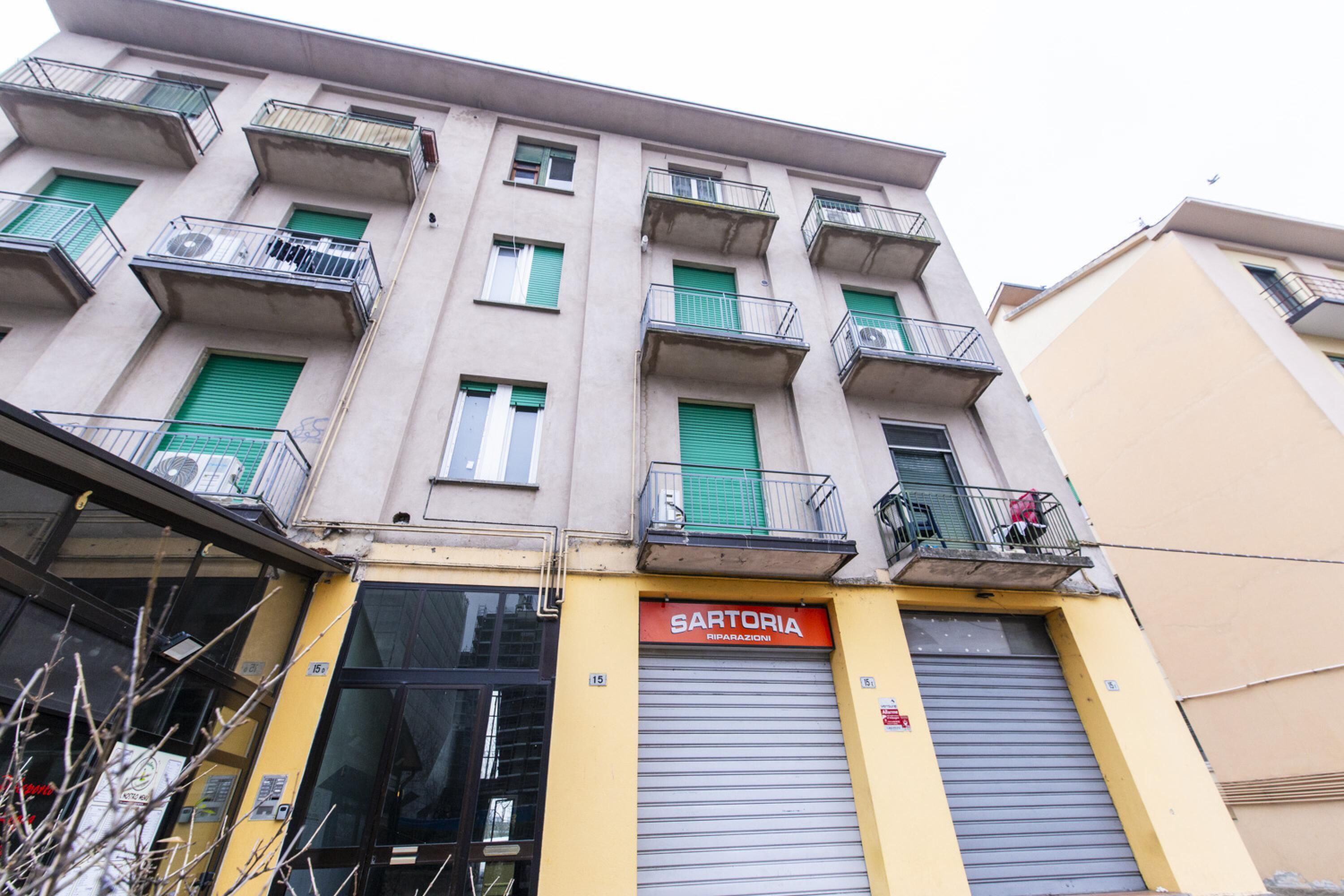 A multi-story building with a storefront labeled "SARTORIA RIPARAZIONI".