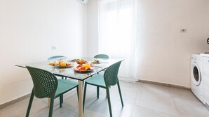 A dining area with a glass table, two chairs, and a washing machine in the corner.