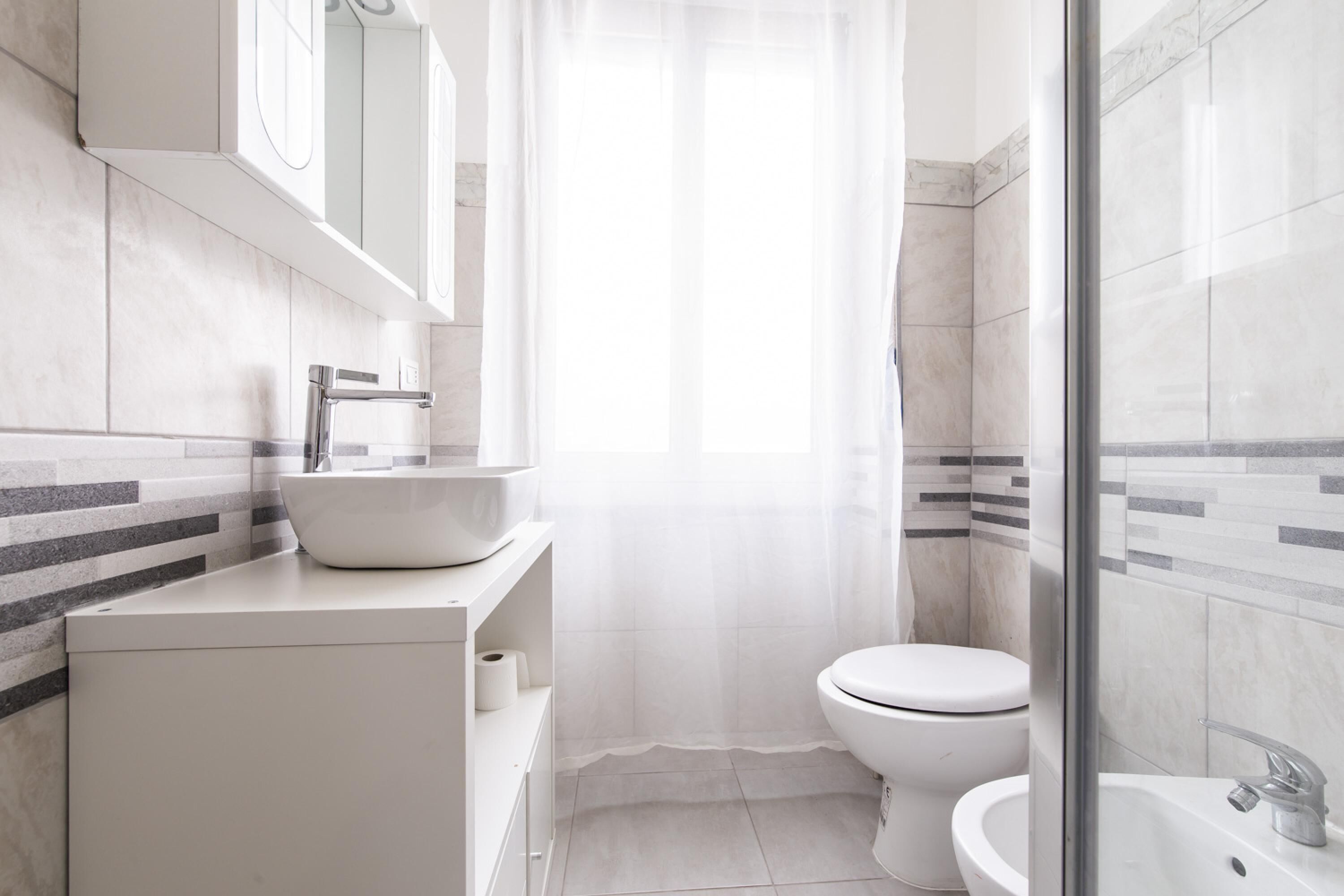 Un baño moderno con lavamanos, inodoro y zona de ducha blancos.