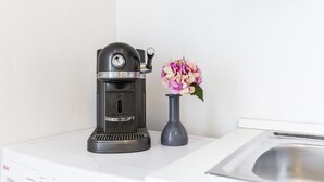A coffee maker on a white countertop next to a vase with flowers.