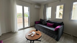 A modern living room with a grey sofa, a wooden coffee table, and a balcony with a view. - Michael Apartments - Private Parking (Lefkada)