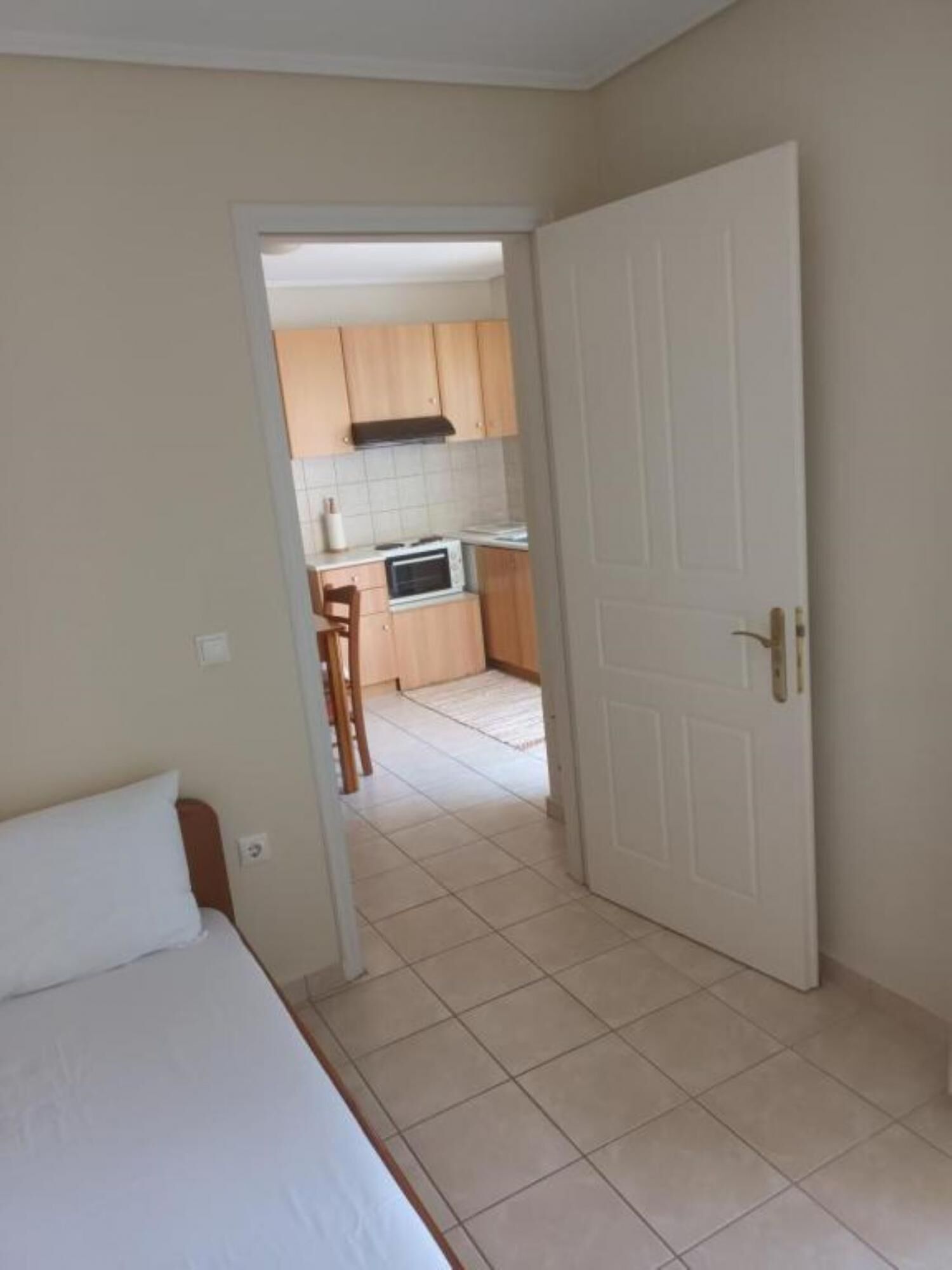Quarto com cama e vista para uma cozinha com micro-ondas e armários de madeira.