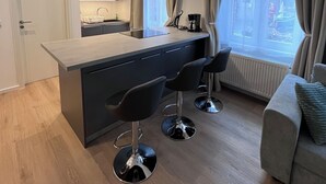 Une cuisine moderne dotée d’un îlot central, de tabourets de bar noirs, d’un canapé et d’une grande fenêtre agrémentée de rideaux.
