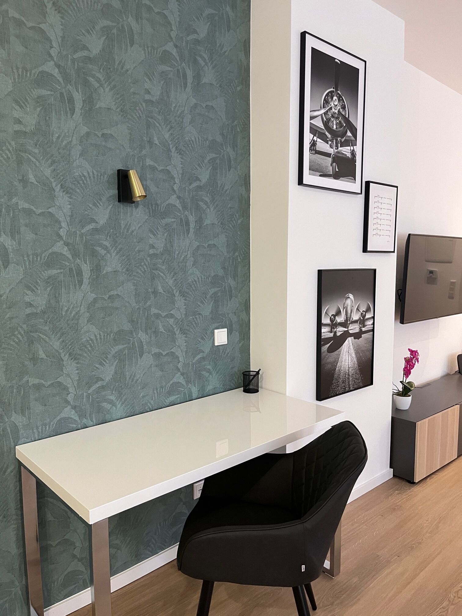 Un espacio de oficina moderno con un escritorio blanco, una silla negra y una pared con estampado verde.