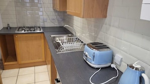 A compact kitchen with a gas stove, a sink with a dish rack, a toaster, and a kettle. - Impeccable 4-bed House in Leicester (Leicester)