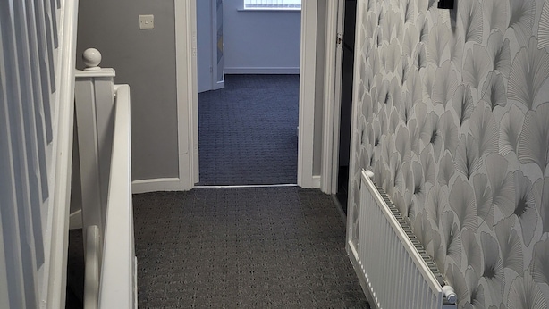 A hallway with a patterned wall, a radiator, and a door leading to another room. - Impeccable 4-bed House in Leicester (Leicester)