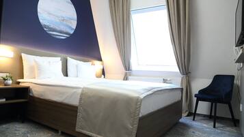 A hotel room with a bed, a chair, a nightstand, a lamp, a window with curtains, and a wall with a circular artwork.