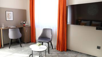 A hotel room with a desk, two chairs, a TV, and a window with curtains.