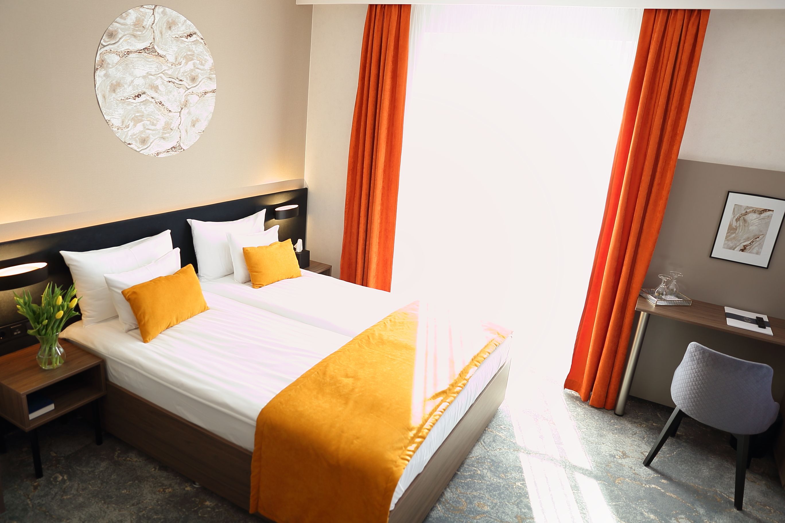 A hotel room with a bed, nightstand, desk, chair, and a wall-mounted artwork.