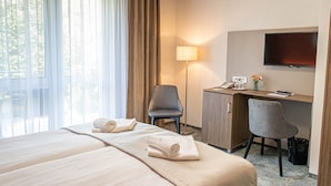 Une chambre d’hôtel avec deux lits, un bureau, une chaise, une télévision et une lampe.