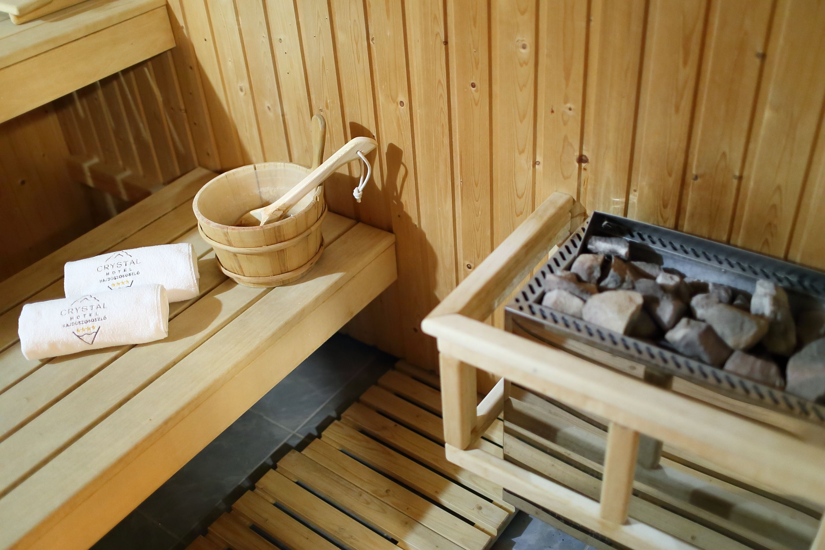 Un sauna en bois avec un banc en bois, un récipient en bois et une louche, ainsi qu’un plateau de pierres.