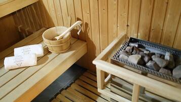 Un sauna en bois avec un banc en bois, un récipient en bois et une louche, ainsi qu’un plateau de pierres.