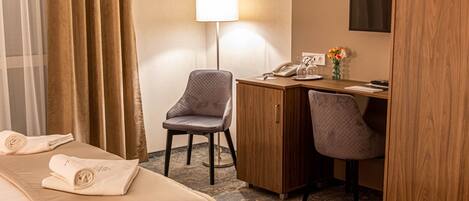 A hotel room with a bed, two chairs, a desk, a lamp, and a small table with flowers.