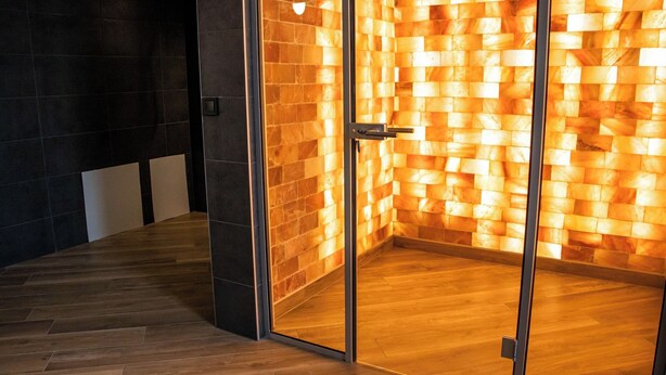 Un intérieur moderne avec un plancher en bois et une porte en verre donnant sur une pièce dont le mur présente une texture chaleureuse.