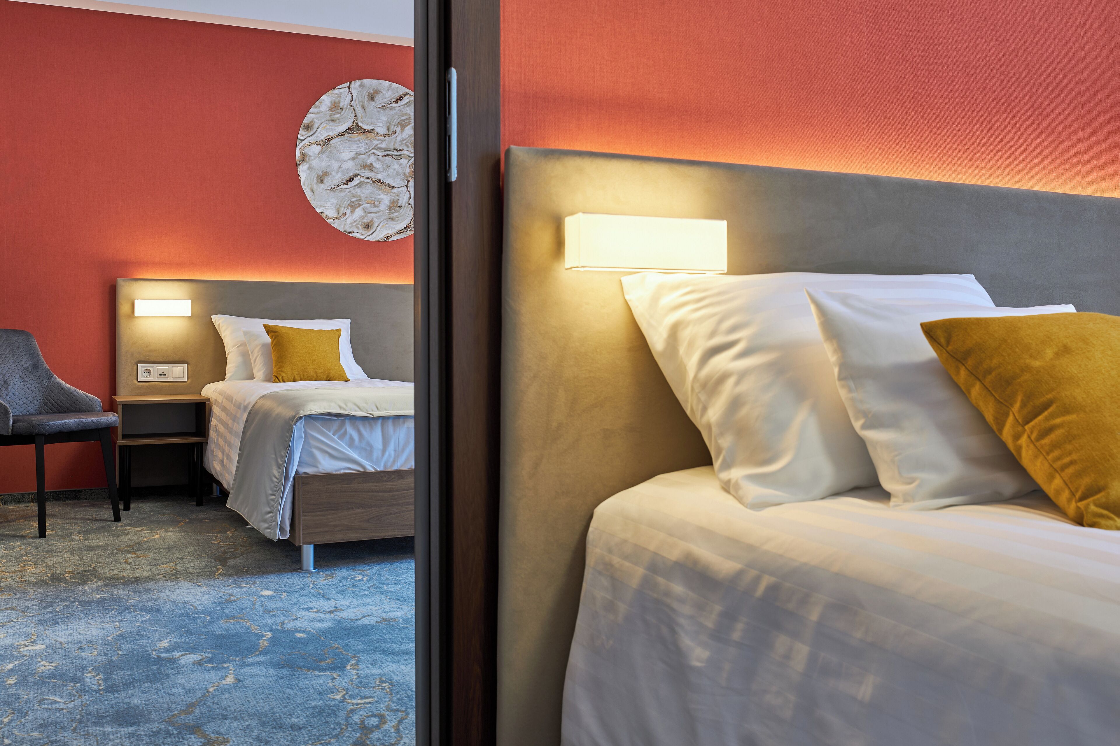 Habitación de hotel con dos camas, una silla, una mesita de noche y una lámpara fijada a la pared.