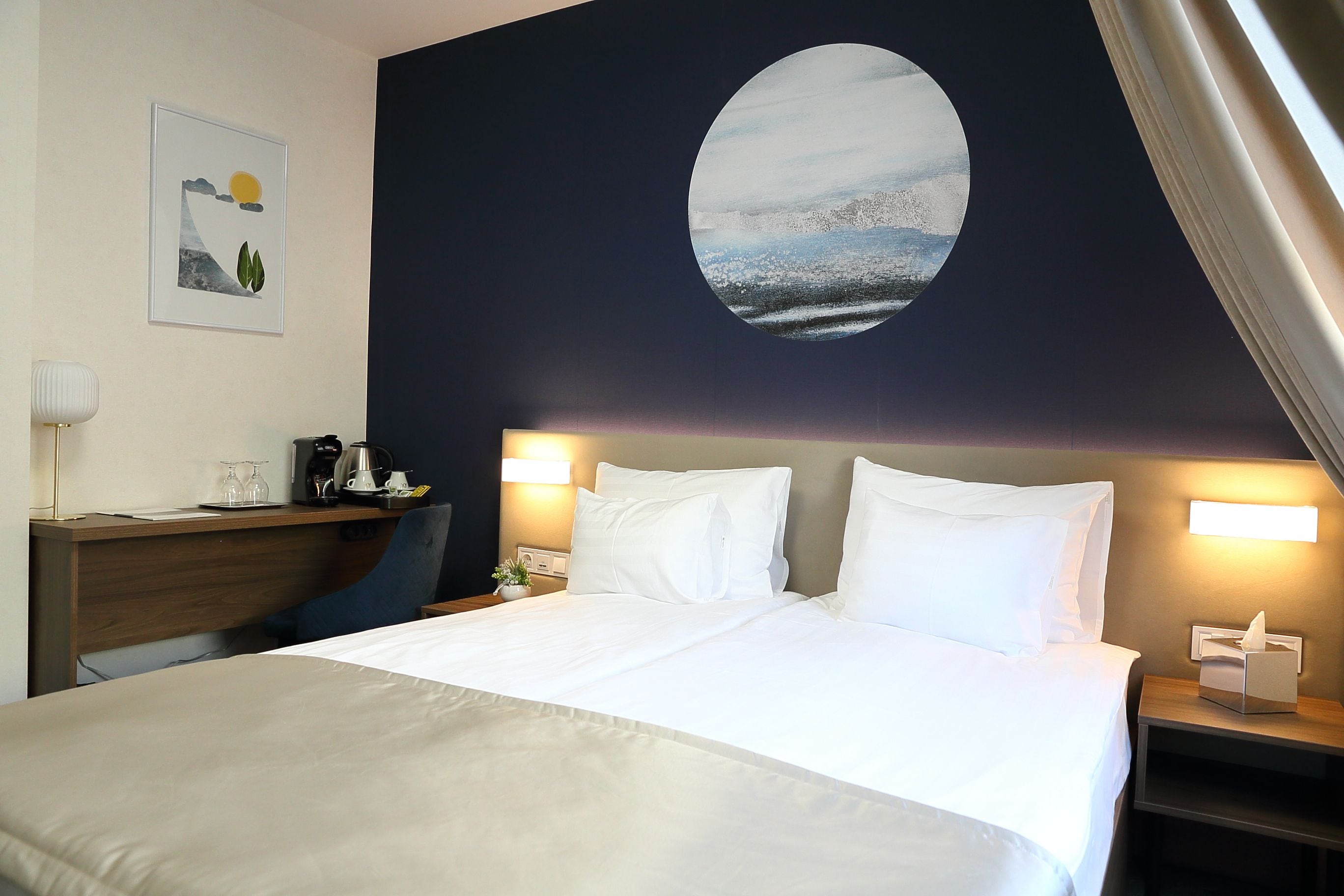Habitación de hotel con cama, escritorio, silla, mesita de noche y lámpara de pared.