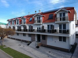 Un edificio residencial de varios pisos con balcones, una escalera y un acceso pavimentado.