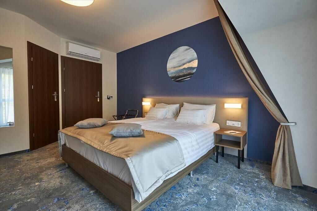 Un dormitorio con una cama, mesitas de noche, un adorno circular en la pared y una ventana.
