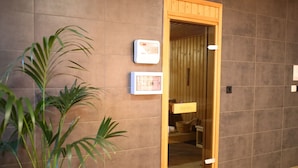 Une porte en bois donne sur une pièce dont le sol est également en bois, où l’on trouve un thermostat fixé au mur et une petite plante.
