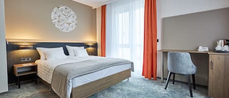A hotel room with a bed, desk, chair, and a wall-mounted artwork.