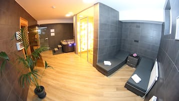 Un spa moderno con piso de madera, una zona de estar con camilla de masaje, una planta pequeña y un panel de vidrio.