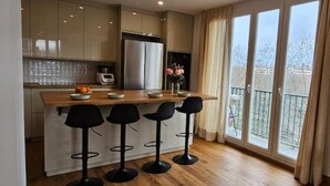 Een moderne keuken met een centraal eiland, barkrukken en uitzicht op een balkon.