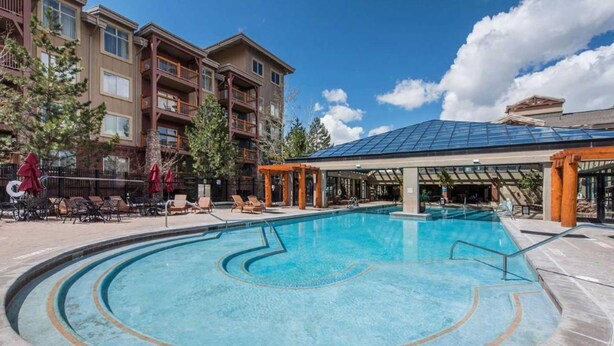 A swimming pool with a sunken center, surrounded by lounge chairs and umbrellas, with a building featuring balconies in the background. - Alpine Abode at Canyons Village | Ski-In/Out Condo (Park City)