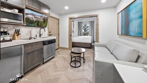 A modern kitchen with stainless steel appliances, a dining area with a white table and a sofa, and a large window with a mountain view. - Alpine Abode at Canyons Village | Ski-In/Out Condo (Park City)