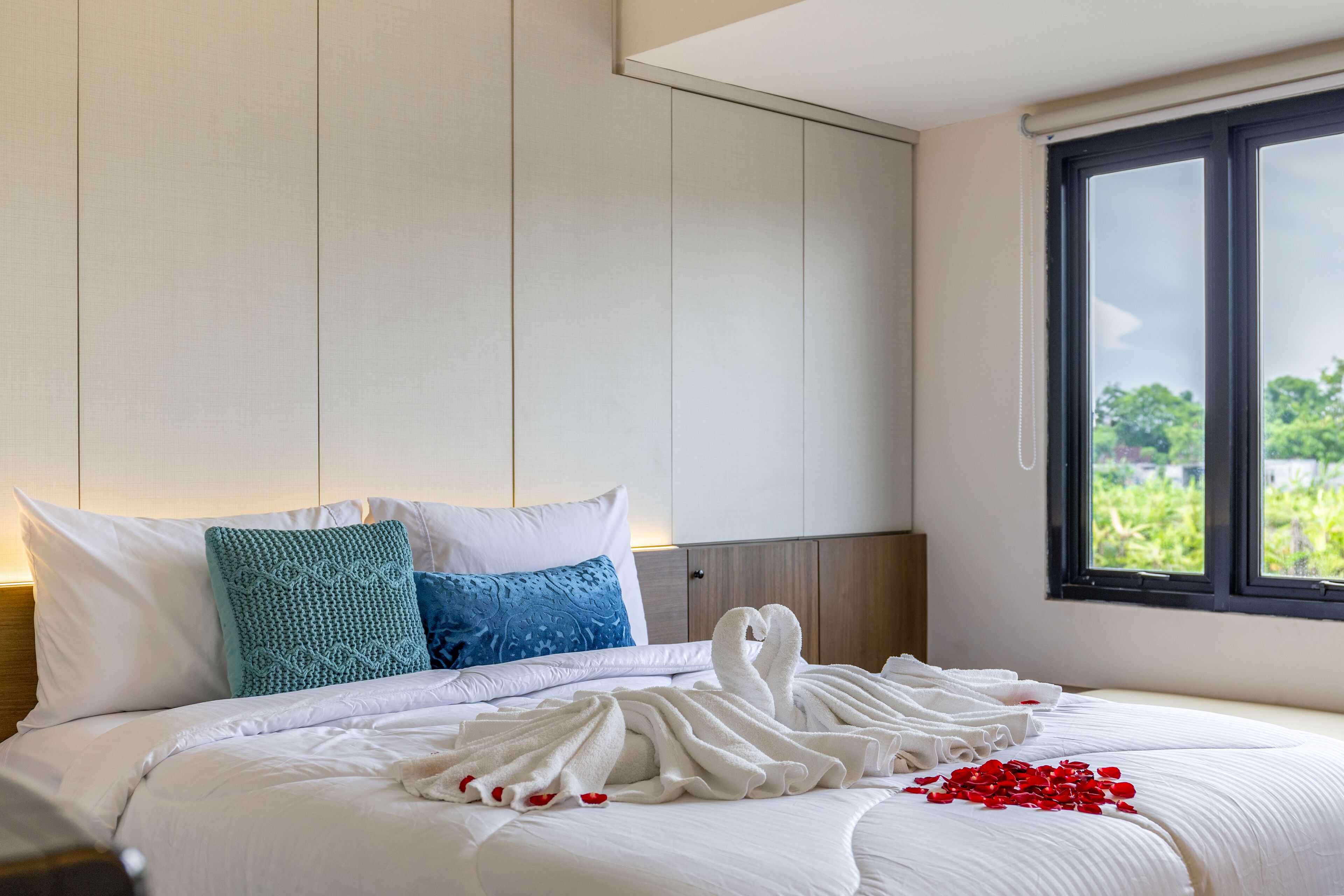 A neatly made bed with white linens, a teal and blue pillow, and a white towel arrangement.